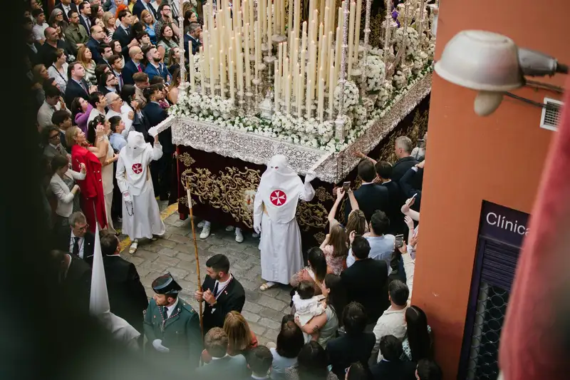 A colorful Holy Week procession with traditional attire in Seville, Spain.